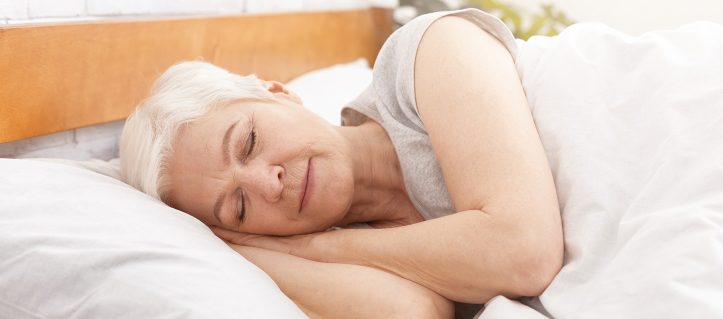 Femme âgée aux cheveux blancs dormant dans son lit.