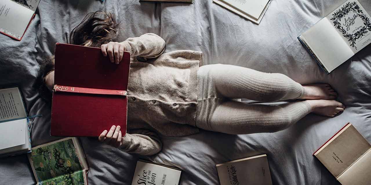 niña tumbada en cama con libros