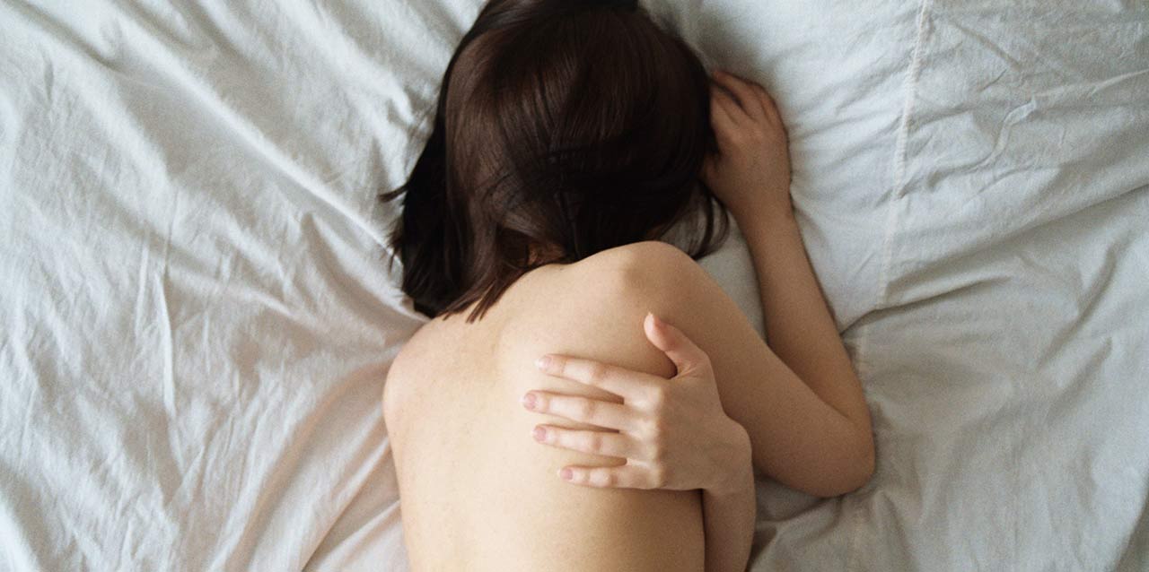 mujer tumbada en cama abrazándose