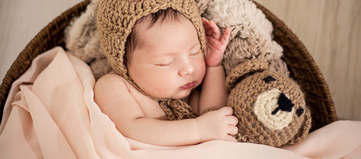 bebe dentro de una cuna de mimbre tapado con sabana beige y gorrito de punto beige durmiendo y soñando junto a su ojo de peluche