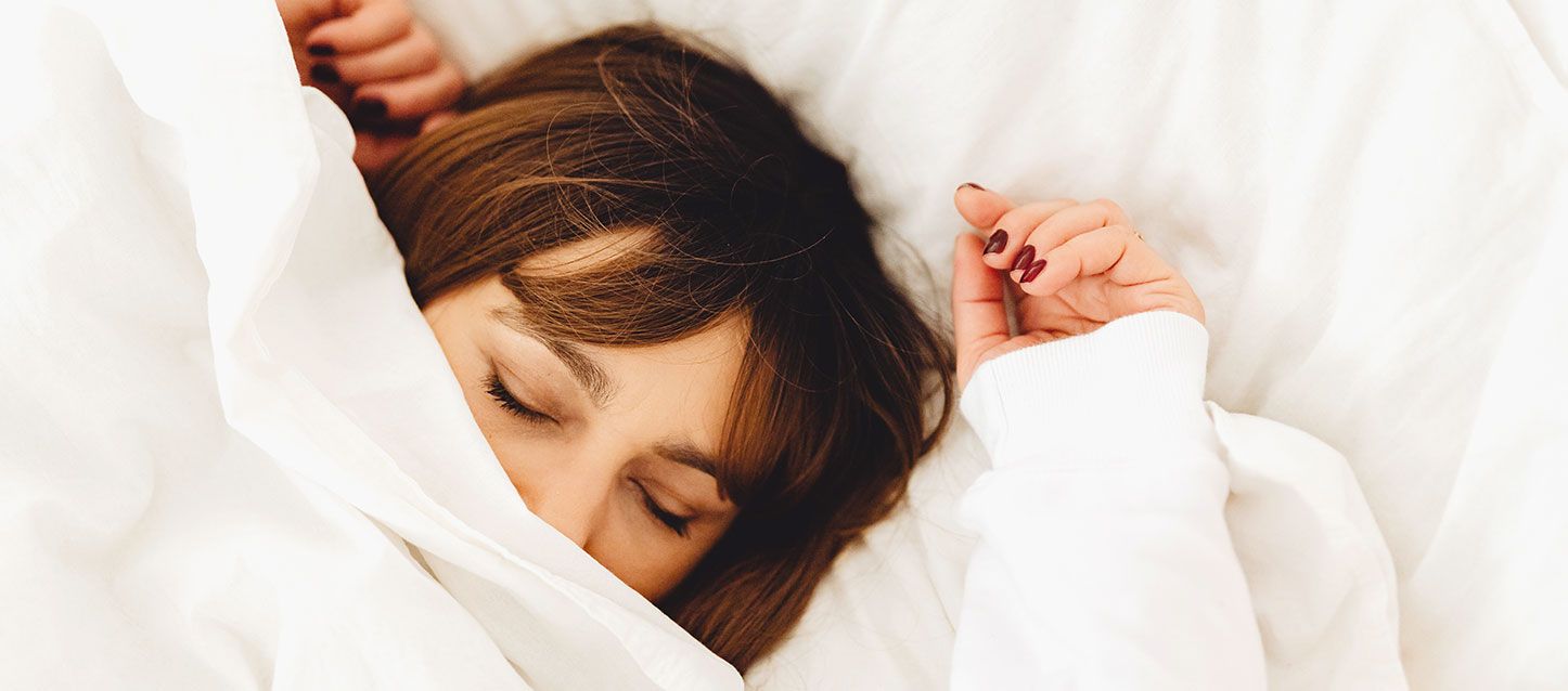 mujer de pelo castaño dormida dentro de la cama tapada con el edredon hasta la nariz