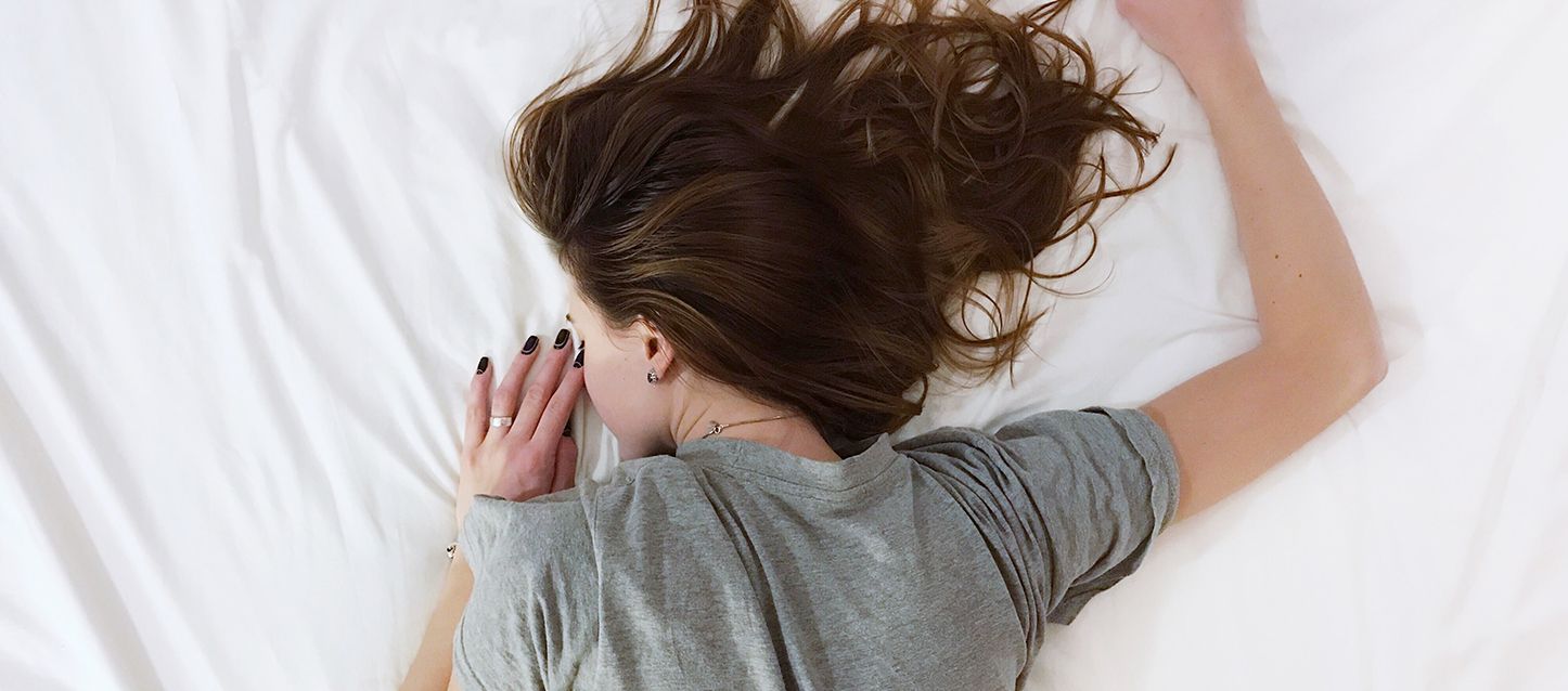 chica de pelo largo moreno y camiseta gris durmiendo boca abajo en la cama con la copa menstrual
