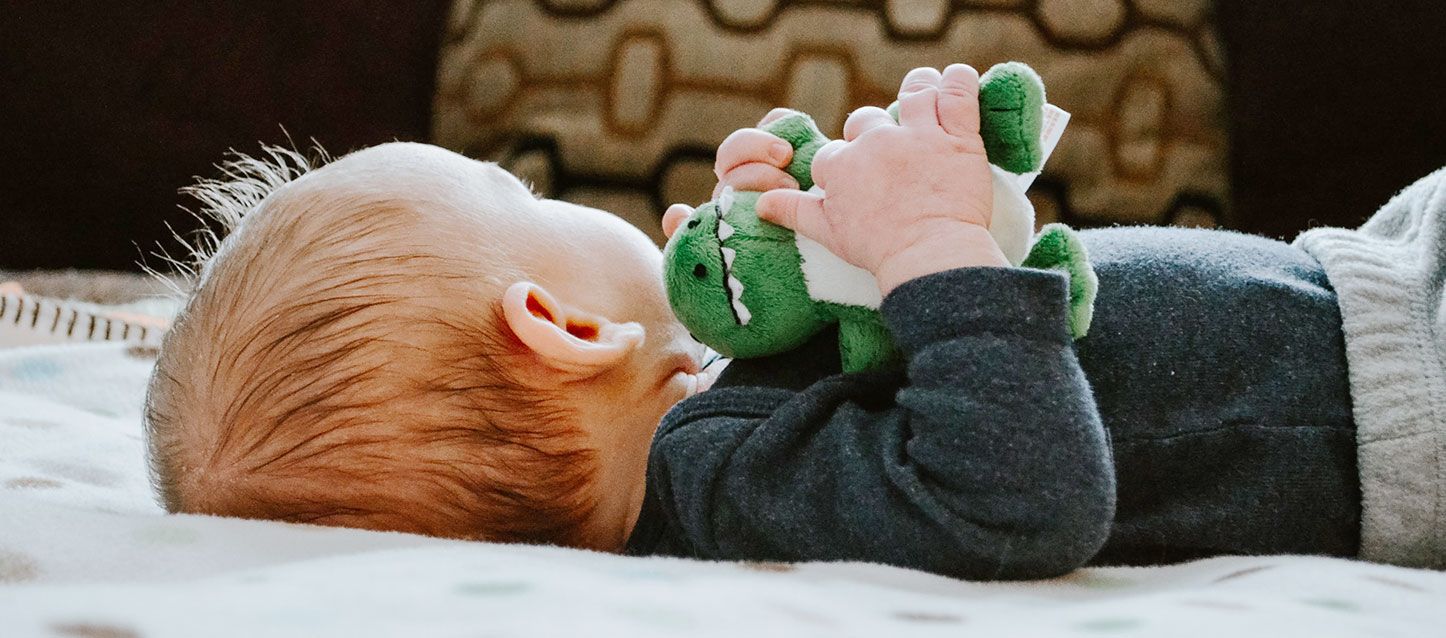 bebe tumbado boca arriba con pijama de felpa negra con una dinosaurio de peluche entre las manos