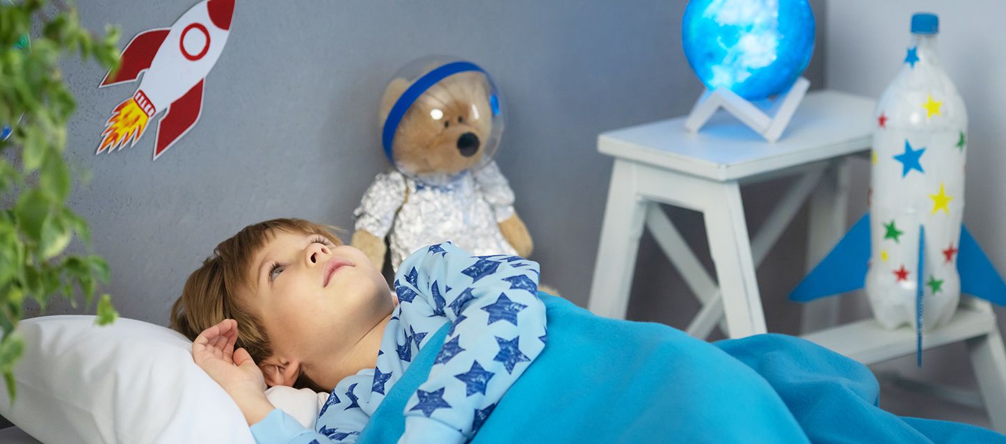 niño con sonambulismo con pijama azul claro con estrellas azul marino metido en la cama despierto en su habitación