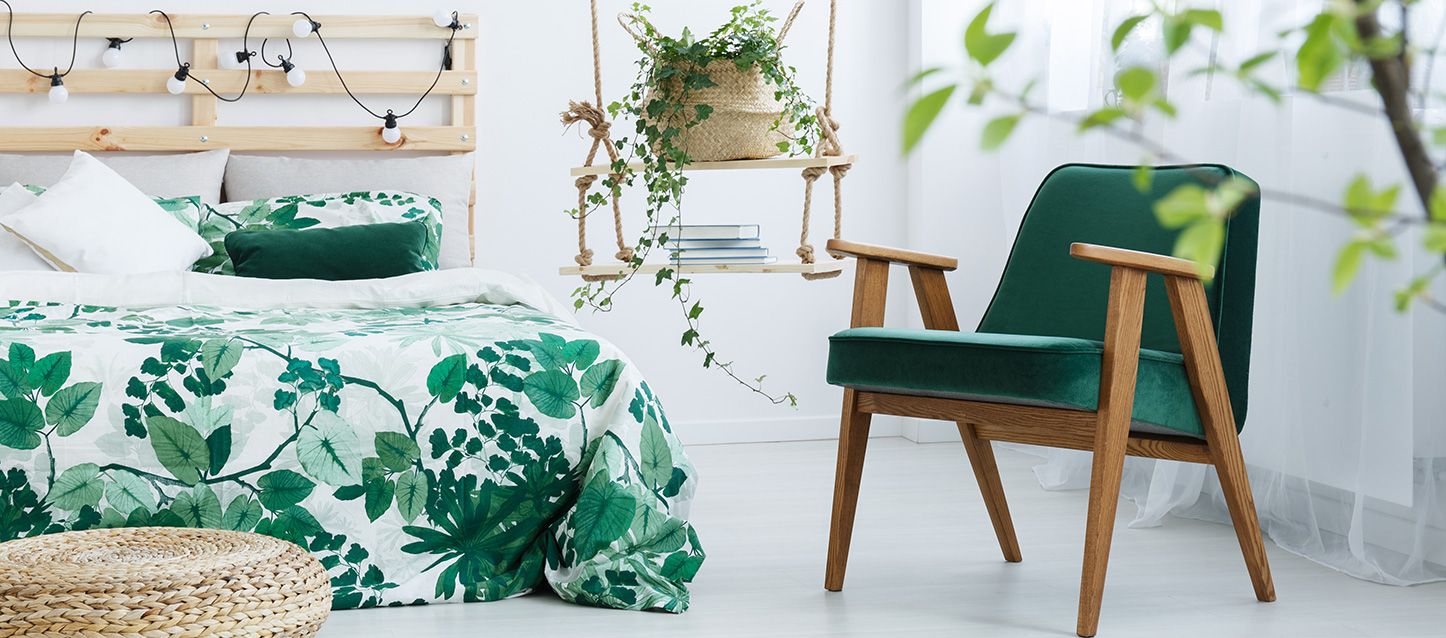 dormitorio verde aguacon edredon con motivos de hojas y plantas, cabecero de palets, silla y estanteria