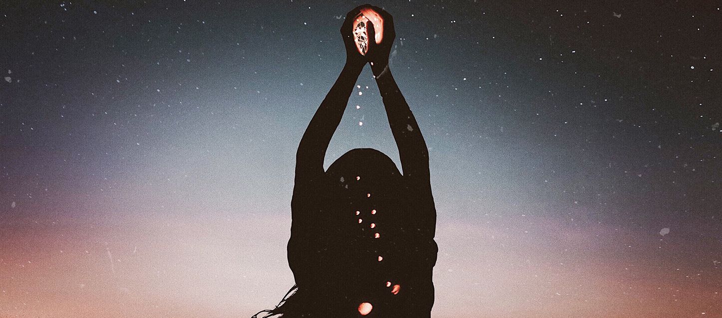 mujer con las manos en el aire al anochecer con luces entre sus manos