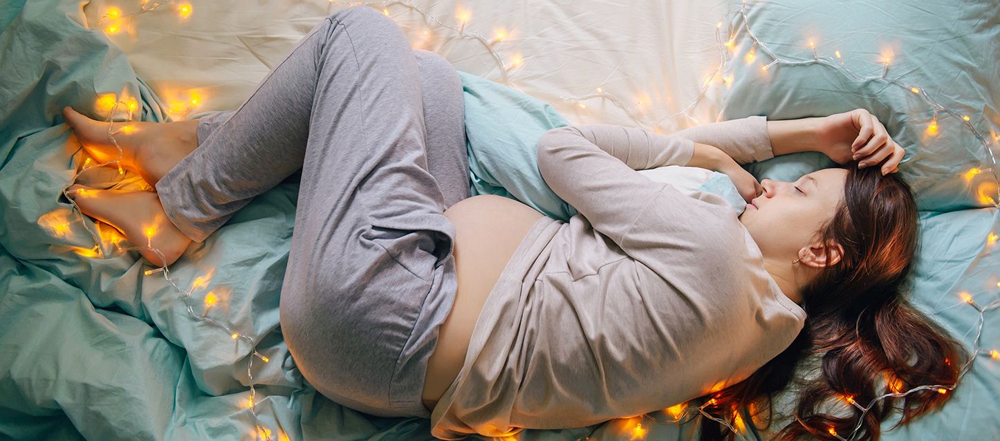 mujer embarazada acosta en la cama de lado abrazando una almohada