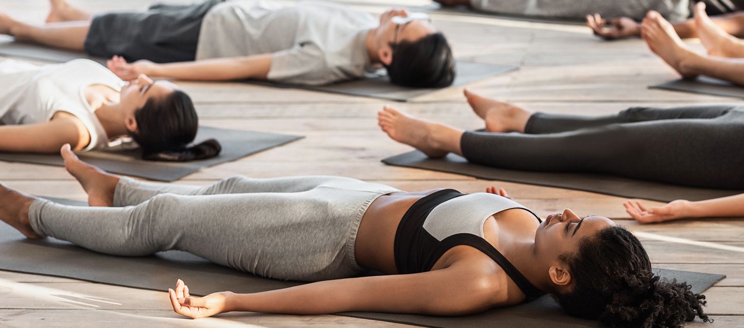 6 personas tumbadas boca arriba en el suelo sobre una esterilla con los ojos cerrados practicando yoga nidra