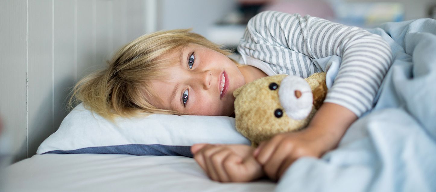 menino loiro metido na cama, de lado, desperto e a abraçar o seu ursinho de peluche