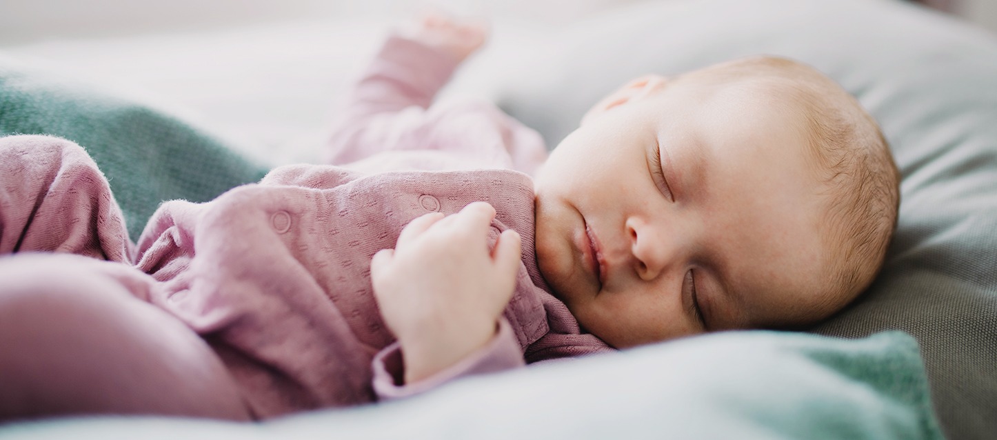 bebé a dormir de barriga para cima, com um pijama violeta